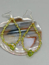 Load image into Gallery viewer, These natural peridot chips earrings feature a gold glass beading on their hoops, creating an eye-catching light green tone. A pressed glass leaf charm is also included, boasting an iridescent shimmer finish with subtle hints of gold, purple, blue, and pink. Measurements: 2 1/2&quot; length
