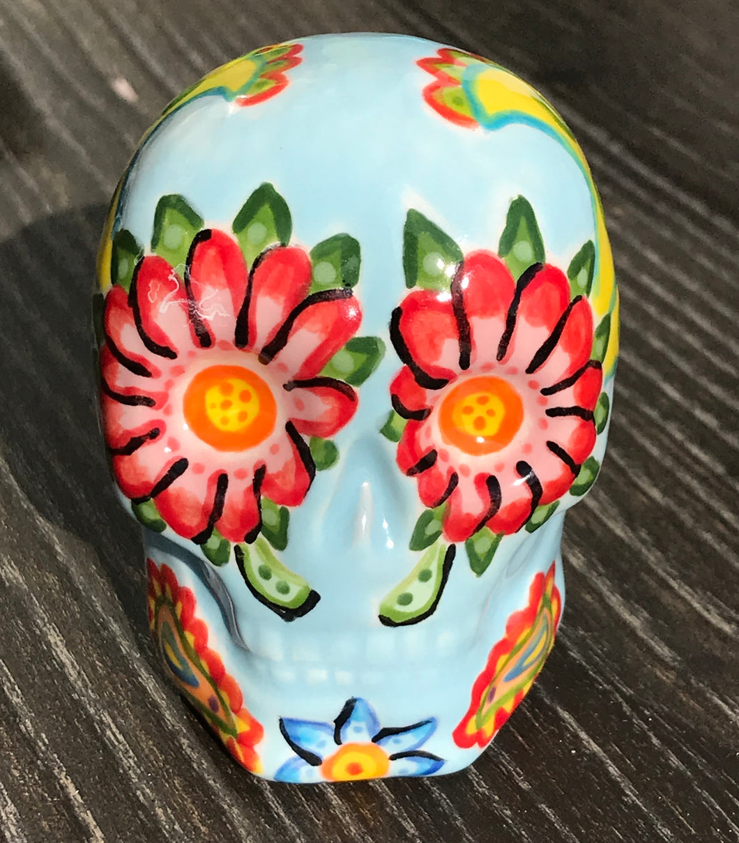 This ceramic skull statuette is a stunning piece of art inspired by nature. Its soft periwinkle blue hue is decorated with multi-color floral motifs, hearts, leaves and colorful accents, creating a beautiful piece of hand-painted, Day of the Dead-themed art.  H 2 3/4” x W 2” x D 2”