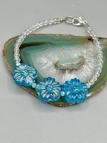 This light blue pressed glass floral bracelet is a sophisticated addition to any summer look. Its iridescent shimmer finish adds a classy touch to its intricate metal wire and lobster claw clasp. Perfect for any nature-inspired wardrobe. Measurements:  Bracelet: 8