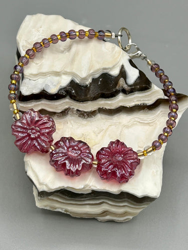 This light purple-pink pressed glass floral beaded bracelet offers delightful detailing with its iridescent shimmer finish. Constructed with metal wire and a lobster claw clasp for secure closure.  Measurements:  Bracelet: 8