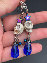Load image into Gallery viewer, Mini Howlite Skull Bead Earrings large star shaped rainbow hematite bead with a large bright blue teardrop shaped glass bead on the bottom of the skull for max shimmer and movement. Ultimate Chingona, Cabrona, Latina Chicana, Goth, Vampire Goth, Dark Witchy, La Bruja Style. You can dress these up or down, it will definitely give your outfit a unique look. You can dress these up or down, it will definitely give your outfit a unique look.  Measurements: 2 ” in length
