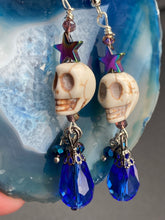 Load image into Gallery viewer, Mini Howlite Skull Bead Earrings large star shaped rainbow hematite bead with a large bright blue teardrop shaped glass bead on the bottom of the skull for max shimmer and movement. Ultimate Chingona, Cabrona, Latina Chicana, Goth, Vampire Goth, Dark Witchy, La Bruja Style. You can dress these up or down, it will definitely give your outfit a unique look. You can dress these up or down, it will definitely give your outfit a unique look.  Measurements: 2 ” in length
