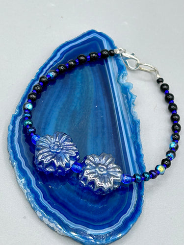 This Dark Blue Violet Pressed Glass Floral Beaded Bracelet features exquisitely detailed components with an iridescent shimmer finish. The piece is crafted with metal wire and a lobster claw clasp.  Measurements:  Bracelet: 8