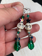 Load image into Gallery viewer, Mini Howlite Skull Bead Earrings large star shaped rainbow hematite bead with a large bright green teardrop shaped glass bead on the bottom of the skull for max shimmer and movement. Ultimate Chingona, Cabrona, Latina Chicana, Goth, Vampire Goth, Dark Witchy, La Bruja Style. You can dress these up or down, it will definitely give your outfit a unique look. You can dress these up or down, it will definitely give your outfit a unique look.  Measurements: 2 ” in length
