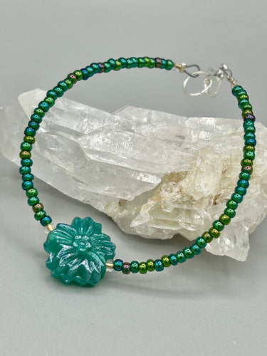 This blue-green pressed glass floral beaded bracelet is a nature-inspired accessory that adds a hint of summer to any look. Crafted with intricate green-blue pressed glass beads and metal wire, the bracelet has an iridescent shimmer finish and a lobster claw clasp for secure wear. Perfect for day-to-night looks. Measurements:  Bracelet: 8 1/2