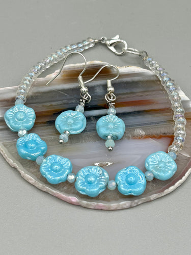 Light blue pressed glass bracelet featuring floral beading is detailed with an iridescent shimmer finish. The bracelet is crafted with metal wire and a lobster claw clasp for easy and secure fastening. Measurements:  Bracelet: 8 1/4