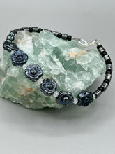 Load image into Gallery viewer, This black metallic floral glass bead and hematite cylinder shaped bracelet is a highly versatile piece; its sleek style can be dressed up or down to match any ensemble. It is constructed of metal wire and features a lobster claw clasp for closing.  Measurements:  Bracelet: 8 1/2&quot; in length 
