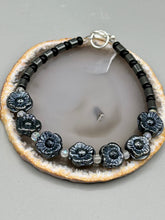 Load image into Gallery viewer, This black metallic floral glass bead and hematite cylinder shaped bracelet is a highly versatile piece; its sleek style can be dressed up or down to match any ensemble. It is constructed of metal wire and features a lobster claw clasp for closing.  Measurements:  Bracelet: 8 1/2&quot; in length 
