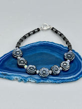 Load image into Gallery viewer, This black metallic floral glass bead and hematite cylinder shaped bracelet is a highly versatile piece; its sleek style can be dressed up or down to match any ensemble. It is constructed of metal wire and features a lobster claw clasp for closing.  Measurements:  Bracelet: 8 1/2&quot; in length 
