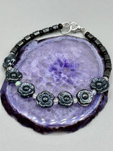 Load image into Gallery viewer, This black metallic floral glass bead and hematite cylinder shaped bracelet is a highly versatile piece; its sleek style can be dressed up or down to match any ensemble. It is constructed of metal wire and features a lobster claw clasp for closing.  Measurements:  Bracelet: 8 1/2&quot; in length 
