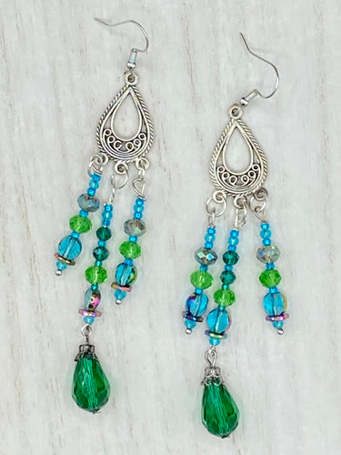This Whimsical Blue Green Peacock Inspired Beaded Earrings set features bold chandelier style earrings with three long strands of glass bead. These show-stopping pieces boast a range of shimmering shades of blue, green, purple, and gold. A perfect addition to any fashionista's collection. Measurements: 3 1/2” in length