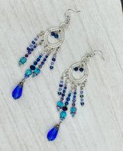 Load image into Gallery viewer, This beautifully large and bold set of chandelier earrings were inspired by the vibrant and beautiful galaxy and cosmos full of bright and stunning hues of blues and purples.  I created this set of earrings with strands of glass beads full of shimmer and bold hues of blues, purples and a tint of gold and greens colors. This is a long, large, and bold piece of jewelry have a lot of shimmer and movement, a “must have” to your collection.   Measurements: 4” in length
