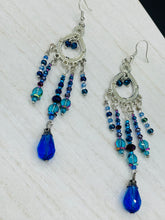 Load image into Gallery viewer, This beautifully large and bold set of chandelier earrings were inspired by the vibrant and beautiful galaxy and cosmos full of bright and stunning hues of blues and purples.  I created this set of earrings with strands of glass beads full of shimmer and bold hues of blues, purples and a tint of gold and greens colors. This is a long, large, and bold piece of jewelry have a lot of shimmer and movement, a “must have” to your collection.   Measurements: 4” in length
