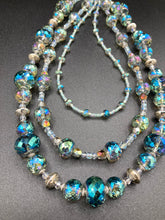 Load image into Gallery viewer, This beautiful necklace features shimmery, rich aqua blue and silver tones glass beads. Its three strands consist primarily of faceted rondelle shaped beads, along with a variety of lighter blue and silver beads, resulting in a unique multicolored look. The perfect statement piece, this elegant necklace will drape beautifully across your neck, adding a vibrant hue to any Spring outfit.  Measurements:    Necklace is 18” in length
