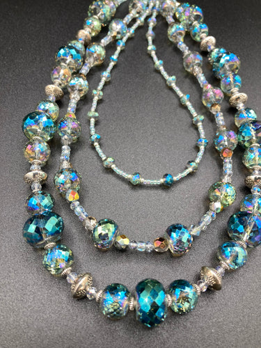 This beautiful necklace features shimmery, rich aqua blue and silver tones glass beads. Its three strands consist primarily of faceted rondelle shaped beads, along with a variety of lighter blue and silver beads, resulting in a unique multicolored look. The perfect statement piece, this elegant necklace will drape beautifully across your neck, adding a vibrant hue to any Spring outfit.  Measurements:    Necklace is 18” in length