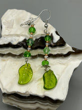 Load image into Gallery viewer, Long strand of glittering light green and gold glass beads, as well as a leaf-shaped glass charm at the bottom, combine to create a highly dynamic effect. These versatile earrings, perfect for a whimsical fairy princess, good witch, or nature-loving hippie look, draw on nature-inspired designs, providing the ideal finishing touch to any ensemble.  Measurements: 2 1/4” in length
