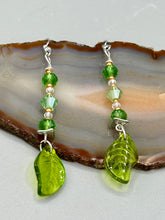 Load image into Gallery viewer, Long strand of glittering light green and gold glass beads, as well as a leaf-shaped glass charm at the bottom, combine to create a highly dynamic effect. These versatile earrings, perfect for a whimsical fairy princess, good witch, or nature-loving hippie look, draw on nature-inspired designs, providing the ideal finishing touch to any ensemble.  Measurements: 2 1/4” in length
