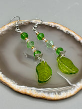 Load image into Gallery viewer, Long strand of glittering light green and gold glass beads, as well as a leaf-shaped glass charm at the bottom, combine to create a highly dynamic effect. These versatile earrings, perfect for a whimsical fairy princess, good witch, or nature-loving hippie look, draw on nature-inspired designs, providing the ideal finishing touch to any ensemble.  Measurements: 2 1/4” in length

