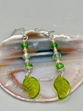 Load image into Gallery viewer, Long strand of glittering light green and gold glass beads, as well as a leaf-shaped glass charm at the bottom, combine to create a highly dynamic effect. These versatile earrings, perfect for a whimsical fairy princess, good witch, or nature-loving hippie look, draw on nature-inspired designs, providing the ideal finishing touch to any ensemble.  Measurements: 2 1/4” in length
