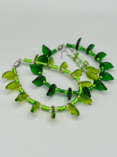 Load image into Gallery viewer, Long strand of glittering light green and gold glass beads, as well as a leaf-shaped glass charm at the bottom, combine to create a highly dynamic effect. These versatile earrings, perfect for a whimsical fairy princess, good witch, or nature-loving hippie look, draw on nature-inspired designs, providing the ideal finishing touch to any ensemble.  Measurements: 2 1/4” in length
