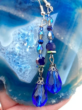 Load image into Gallery viewer, This stunning, one of a kind pair of celestial beaded earrings is a bold addition to any jewelry collection. Crafted with vibrant blue glass beads, the color contains varied shades of blue, purple, and hints of gold to create unique texture. The design is inspired by the awe-inspiring beauty of the majestic galaxy.  Measurements: 2” in length
