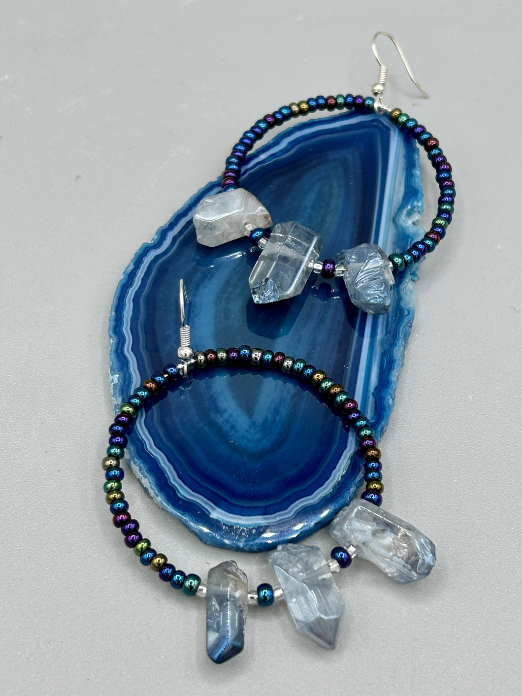 These ultra-trendy crystal nugget and glass beaded hoop earrings are perfect for any hippie or bohemian look. The dark blue glass beads give off an iridescent shimmer and blend brilliantly with the luster blue crystals, creating an eye catching contrast and a unique touch of nature-inspired beauty. Measurements: 2 1/4