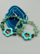 Load image into Gallery viewer, This pair of earrings features a turquoise magnesite floral bead with a vibrant orange glass bead and natural green aventurine stone chips juxtaposed against gold and blue glass beads. Measurements: 2" length 
