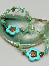 Load image into Gallery viewer, This pair of earrings features a turquoise magnesite floral bead with a vibrant orange glass bead and natural green aventurine stone chips juxtaposed against gold and blue glass beads. Measurements: 2" length 
