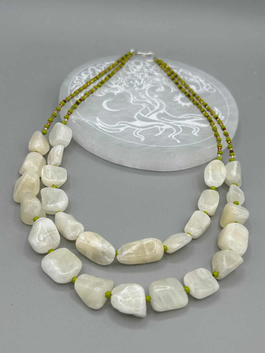 This exquisite necklace features large natural Calcite beads complemented by Wasabi Green glass beads. Two strands of neutral colors bring a sophisticated look that can dress up or dress down any outfit for a one-of-a-kind style.    Measurements:    Necklace is 17 1/4 