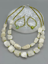 Load image into Gallery viewer, These natural peridot chips earrings feature a gold glass beading on their hoops, creating an eye-catching light green tone. A pressed glass leaf charm is also included, boasting an iridescent shimmer finish with subtle hints of gold, purple, blue, and pink.  Measurements: 2 1/2&quot; length
