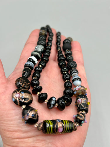 Add flair to your look with this unique large and chunky hand beaded necklace. Featuring a wide variety of mixed black glass beads in different sizes and shapes, this intricately-crafted statement piece offers a bold, hippie-chic, shabby-chic, and bohemian style.  Measurements:  Necklace is 18” in length, can be adjusted up to 20