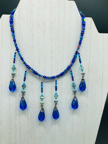 This Victorian Gothic Cobalt Blue Glass Beaded Choker Style Necklace is a true showstopper, with vibrant blue adjustable collar style glass beading and bright dark blue tear drop glass beads. Rainbow hematite beads are added to create a complex and visually-appealing combination of shapes and colors. Necklace is 14” adjustable up to 18