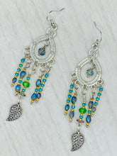 Load image into Gallery viewer, These large chandelier-style earrings feature blues, greens, and iridescent glass beads as well as a finely crafted silver plated leaf charm for added detail. Perfect for bohemian-inspired looks, these versatile earrings can elevate any wardrobe from whimsical hippie to boho chic.  Measurements: 3 1/4” in length

