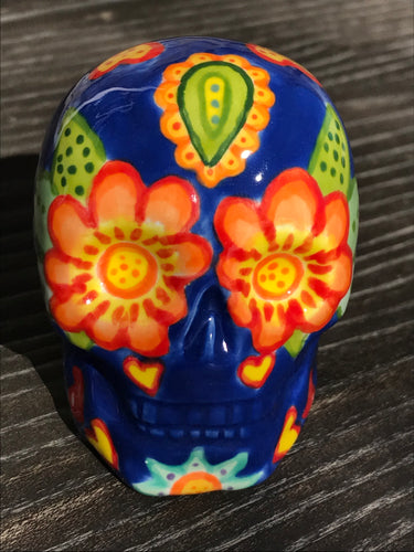 Inspired by nature, this ceramic skull statuette is full of vibrant color and intricate details. The primary color is royal blue with multi-color floral motifs that are painted across the skull, along with hearts and leaves and lively colorful accents around the entire skull. 