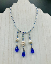 Load image into Gallery viewer, This adjustable collar-style necklace features two shimmery strands of silver and blue glass beads, with three skull charms boasting large, luminous blue teardrop glass beads adding extra shimmer and movement.  Measurements:  Necklace is 14 3/8” adjustable up to 18" in length
