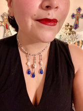 Load image into Gallery viewer, This adjustable collar-style necklace features two shimmery strands of silver and blue glass beads, with three skull charms boasting large, luminous blue teardrop glass beads adding extra shimmer and movement.  Measurements:  Necklace is 14 3/8” adjustable up to 18" in length
