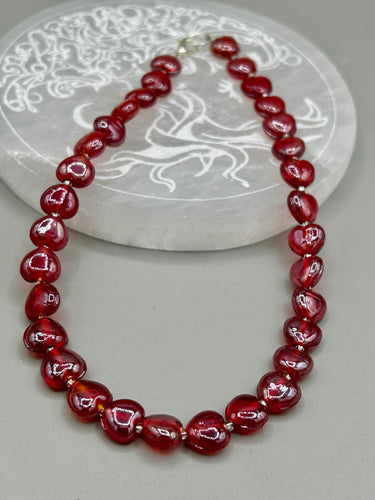 This ruby red heart-shaped glass beaded necklace features a shimmery and vivid iridescent hue, secured with a hook-eye clasp. Measurements:    Necklace is 19