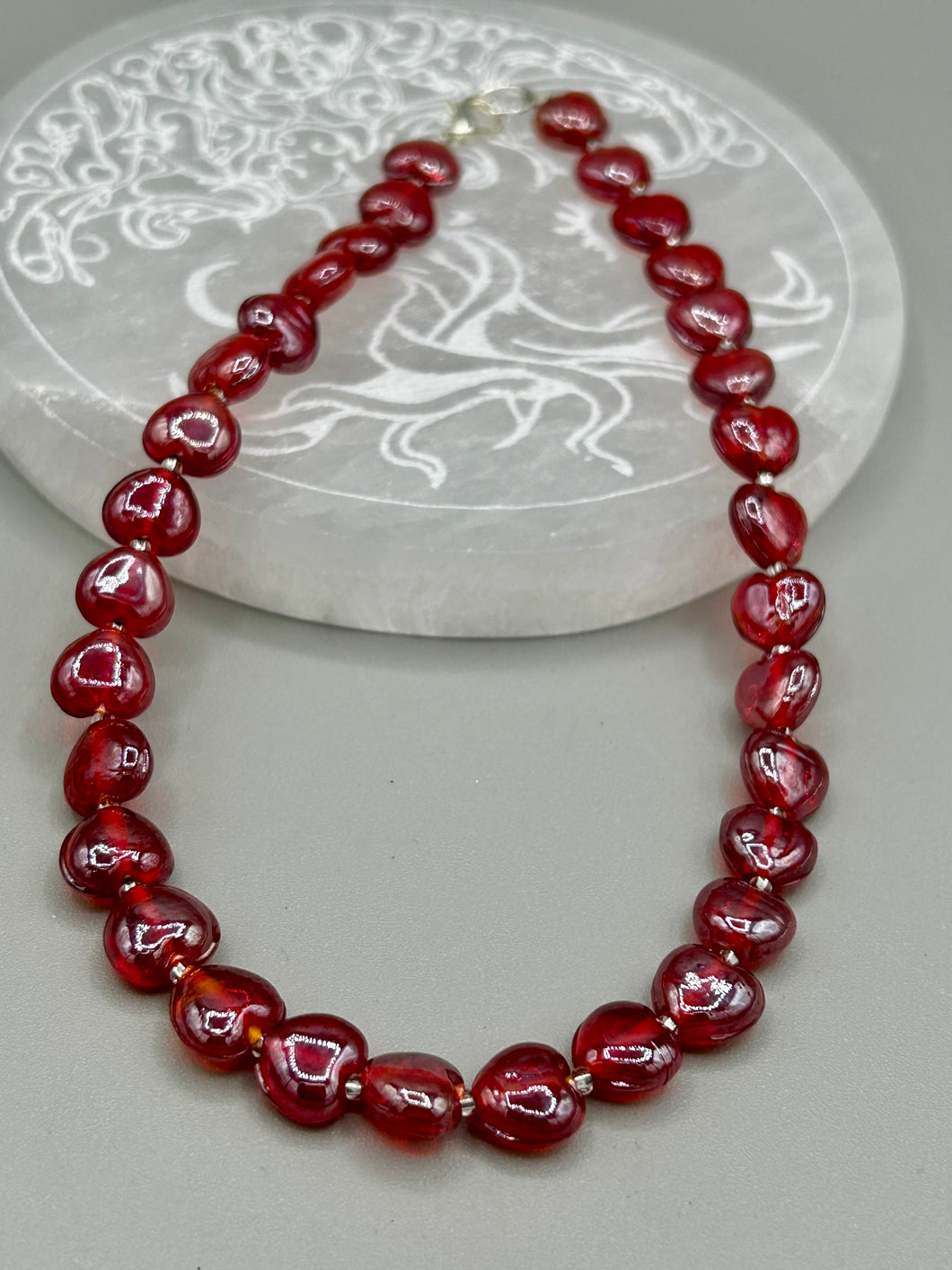 This ruby red heart-shaped glass beaded necklace features a shimmery and vivid iridescent hue, secured with a hook-eye clasp. Measurements:    Necklace is 19