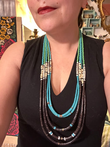 This striking and bold skull necklace is a must-have addition to any jewelry collection. Featuring five strands of glass and bone beads, this hand-beaded necklace is crafted with a combination of beautiful earth-tone colors to complement any outfit.  Measurements:  Necklace:  Shortest strand is 29 1/2” and longest strand 35 1/2