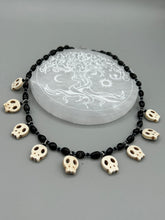 Load image into Gallery viewer, This black and white Goth-style necklace displays a series of shimmering dark-toned glass beads that gracefully encircle the neck and feature hanging skull-shaped beads. A powerful, bewitching and audacious piece of jewelry.  Measurements: 19 1/4&quot;
