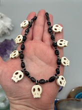 Load image into Gallery viewer, This black and white Goth-style necklace displays a series of shimmering dark-toned glass beads that gracefully encircle the neck and feature hanging skull-shaped beads. A powerful, bewitching and audacious piece of jewelry.  Measurements: 19 1/4&quot;
