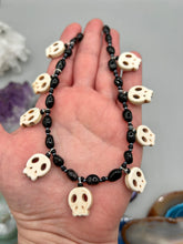 Load image into Gallery viewer, This black and white Goth-style necklace displays a series of shimmering dark-toned glass beads that gracefully encircle the neck and feature hanging skull-shaped beads. A powerful, bewitching and audacious piece of jewelry.  Measurements: 19 1/4&quot;
