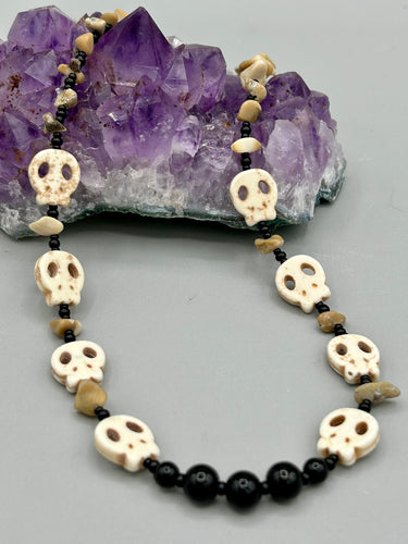 This skully necklace is full of neutral tones and is adorned with natural black obsidian and bamboo chips, as well as small glass beads. It has a unique design that creates a striking silhouette across the wearer's neck. An ideal statement piece for bold fashion enthusiasts.   Measurements:  Necklace - 19 1/4