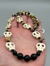 Load image into Gallery viewer, This skully necklace is full of neutral tones and is adorned with natural black obsidian and bamboo chips, as well as small glass beads. It has a unique design that creates a striking silhouette across the wearer&#39;s neck. An ideal statement piece for bold fashion enthusiasts.   Measurements:  Necklace - 19 1/4&quot;
