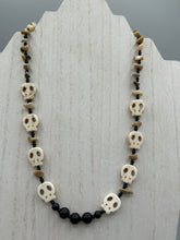 Load image into Gallery viewer, This skully necklace is full of neutral tones and is adorned with natural black obsidian and bamboo chips, as well as small glass beads. It has a unique design that creates a striking silhouette across the wearer&#39;s neck. An ideal statement piece for bold fashion enthusiasts.   Measurements:  Necklace - 19 1/4&quot;
