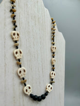 Load image into Gallery viewer, This skully necklace is full of neutral tones and is adorned with natural black obsidian and bamboo chips, as well as small glass beads. It has a unique design that creates a striking silhouette across the wearer&#39;s neck. An ideal statement piece for bold fashion enthusiasts.   Measurements:  Necklace - 19 1/4&quot;
