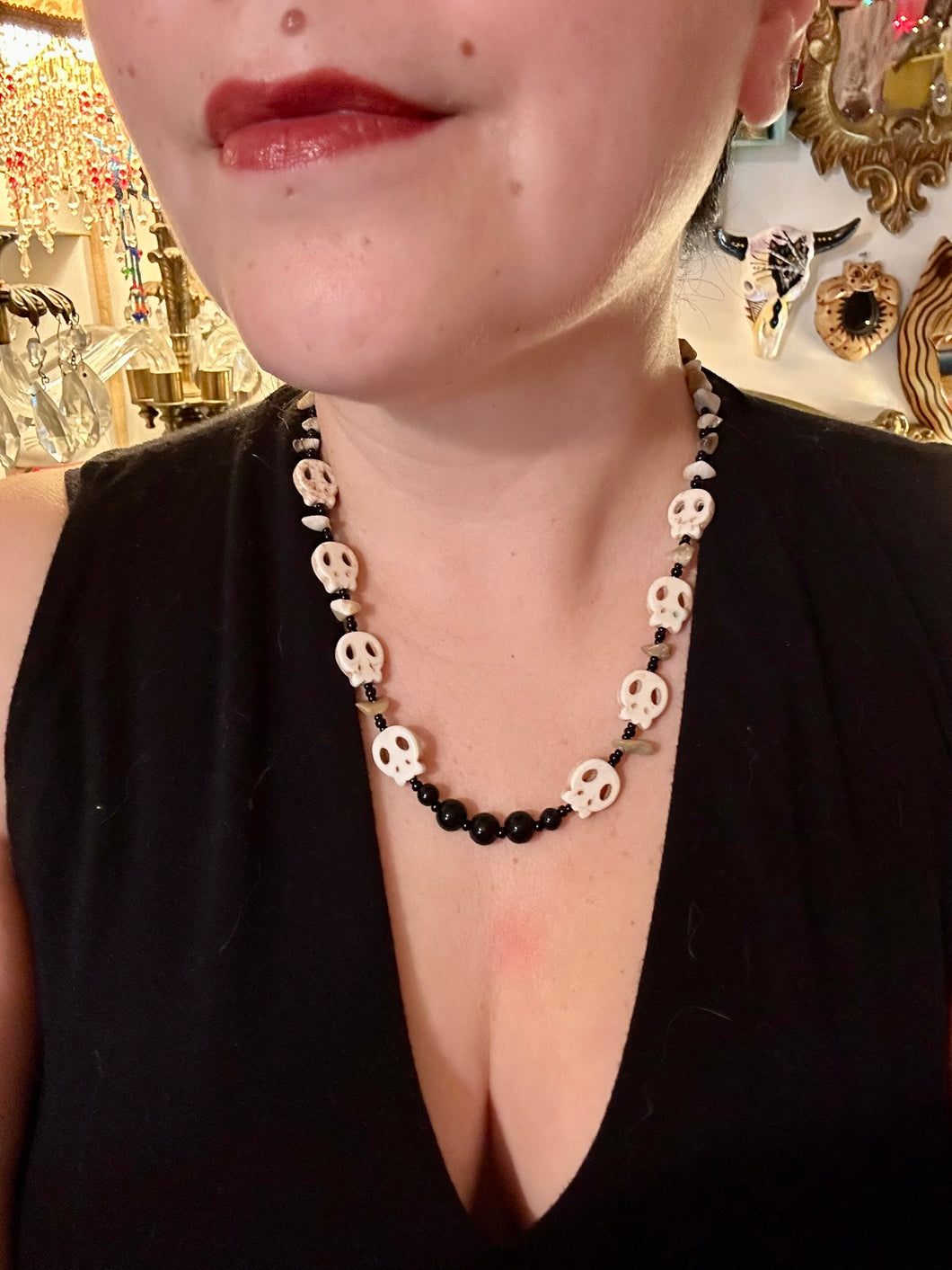 This skully necklace is full of neutral tones and is adorned with natural black obsidian and bamboo chips, as well as small glass beads. It has a unique design that creates a striking silhouette across the wearer's neck. An ideal statement piece for bold fashion enthusiasts.   Measurements:  Necklace - 19 1/4