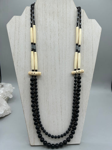 This two-strand necklace features a selection of natural black obsidian stone, hematite, bone, and glass beads. This neutral-hued accessory enhances any ensemble.  Measurements:   Necklace is 29” in length, can be adjusted up to 30