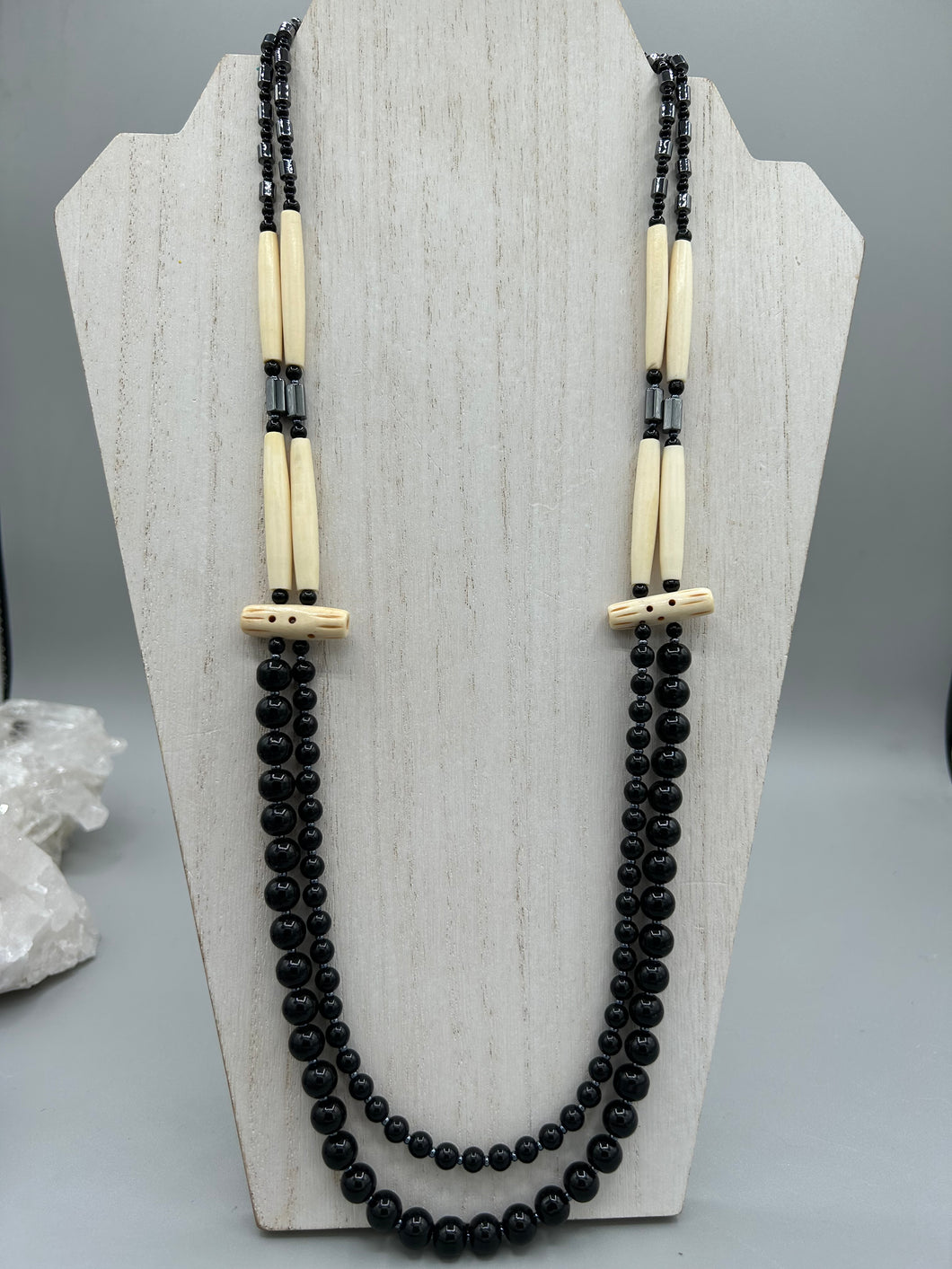 This two-strand necklace features a selection of natural black obsidian stone, hematite, bone, and glass beads. This neutral-hued accessory enhances any ensemble.  Measurements:   Necklace is 29” in length, can be adjusted up to 30