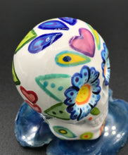 Load image into Gallery viewer, Inspired by nature, this ceramic skull statuette is full of vibrant color and intricate details that I hand painted. The primary color is white with multi-color floral motifs that are painted across the skull, along with hearts and leaves and lively colorful accents around the entire skull. 
